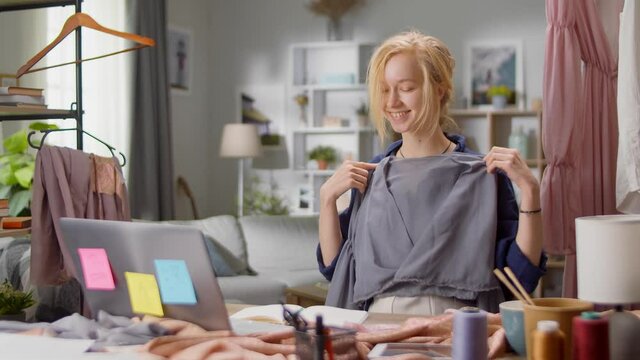 Beautiful young woman fashion designer communicates with the client via video call at home in the living room