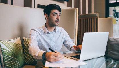 Pensive businessman typing on laptop and doing paperwork