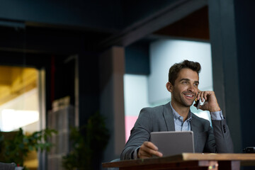 Smiling businessman using a tablet and talking on his cellphone