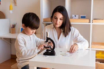 Kid exploring science with a microscope and mother or teacher help. Homeshooling. Learning Community. Montessori School