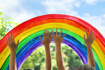 Children touching picture of rainbow on window, closeup. Stay at home concept