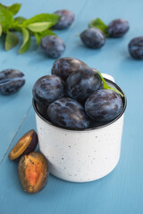 Fresh plums in mug on wooden blue table. New harvest. Close up, vertical