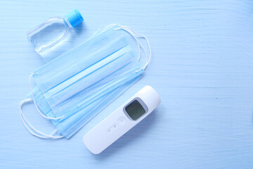 Fototapeta na wymiar Surgical masks, thermometer and hand sanitizer on color background 