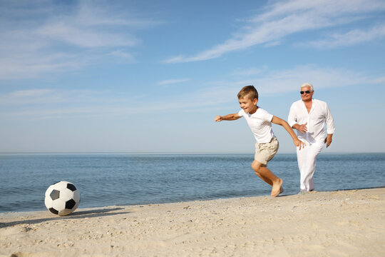 Cute Little Boy With Grandfather Playing Football On Sea Beach