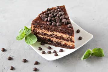 Piece of chocolate cake on a white plate with chocolate droplets and mint leaves