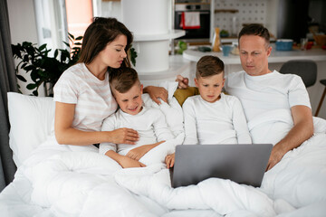 Beautiful parents with kids enjoying at home. Young family watching movie on lap top..