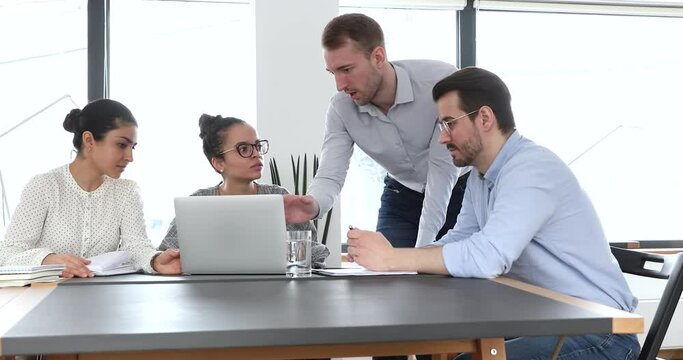 Diverse group gathered in office use laptop discuss new project meeting led by male team leader show new corporate app to colleagues, give useful info helps to workmates with task. Mentoring concept