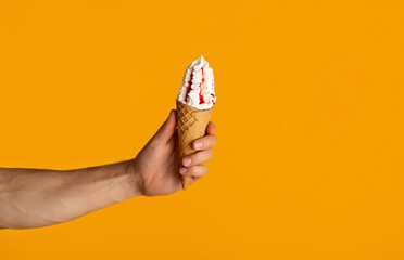 Cropped view of millennial guy holding yummy ice cream in waffle cone over orange background,...