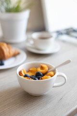 Delicious milk oatmeal with apricots and blueberries in a white bowl on a wooden table in the kitchen. Vertical photo