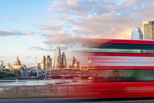A red London bus goes past in a blur across Waterloo Bridge with the City of London and Southbank in distance, London, England
