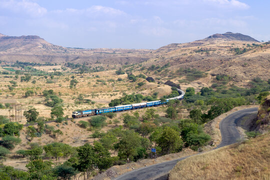 Train on a curved track with background of hills and sky and a foreground road.