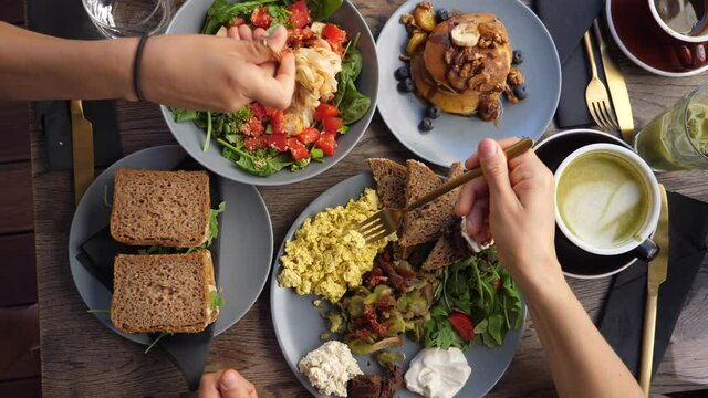 Top view of hands eating healthy organic vegan breakfast of full English, pasta salad and vegan pancakes served on wooden table