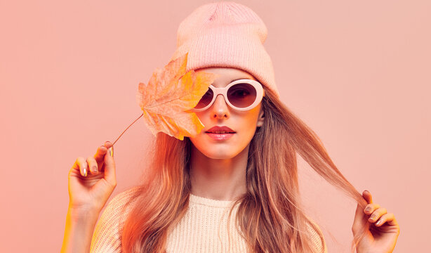 Fashionable hipster woman in Trendy autumn fall outfit, stylish hair, makeup. Blonde model in jumper, fashion jeans having fun smiling. Beautiful girl in autumnal beanie hat with maple leaf