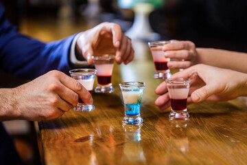Cocktail at the nightclub. Group friends tequila shot glasses in bar. Male hands glasses of shot or liqueur. Friends drink shot or liqueur. Five glasses of alcohol.Tequila shots, vodka, whisky, rum