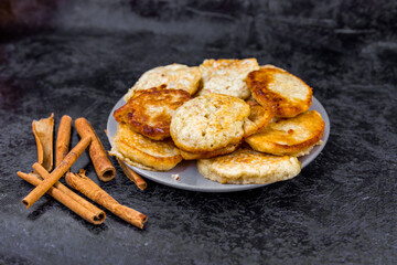 Cinnamon sticks, pancakes, dried fruits and grapes on a dark abstract background with place for text.