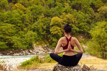 Yoga classes in nature. The concept of playing sports alone. Social exclusion. A woman does yoga on rocks, near a mountain river flows