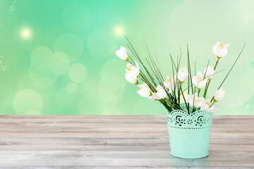 Closeup of bunch of blooming artificial white flower in a decorative green vase on a rustic table over abstract green background. Template for mother day, wedding, valentine, birthday or other holiday