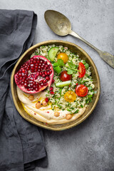 Rustic bowl with couscous salad with vegetables, hummus and fresh cut pomegranate. Middle eastern...