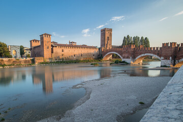 Fototapeta premium Low profile long exposure photo of a Castel vecchio bridge in Verona, Italy on a sunny day. Beautiful brick wall above the river of Adige on a blue sky
