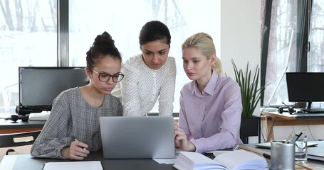Female interns listen indian professional mentor helps to colleagues with corporate app at laptop business program work together in coworking. Boss provide instructions guidance to apprentices concept
