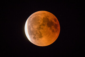 Red or blood moon, full moon eclipse in 2018. Astronomical picture of red moon in an eclipse phase with sun just starting to shine on the left.