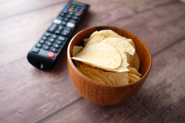 bowl of chips and tv remote on wooden background .