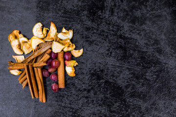 Cinnamon sticks, pancakes, dried fruits and grapes on a dark abstract background with place for text.