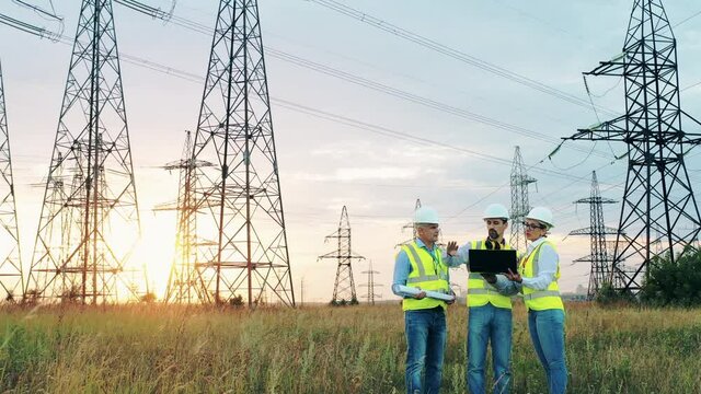 Electric industry, electrical energy production concept. Energy workers discuss work near power lines.