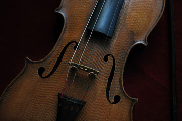 Beautifully designed old violin with missing strings set against a burgundy red velvet background,...