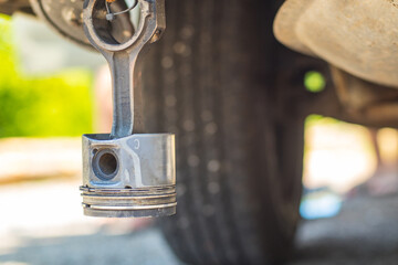 A worn car piston hanging from the  underside of a car as a  souvenir. Joke with destroyed car piston on the undercarriage of another car.