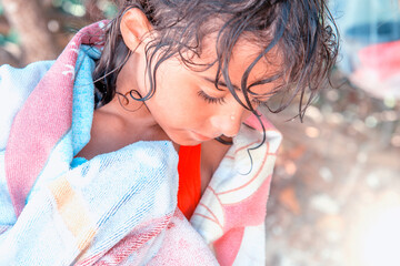 Thinking young girl in her swimsuit, portrait of a six year old at the beach. She is wrapped in a pink towel