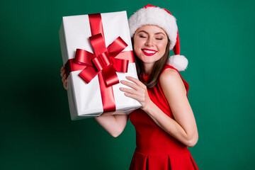 Photo positive charming girl in santa claus headwear receive get x-mas newyear christmas night wish gift box she wait whole year enjoy wear skirt isolated dark green color background