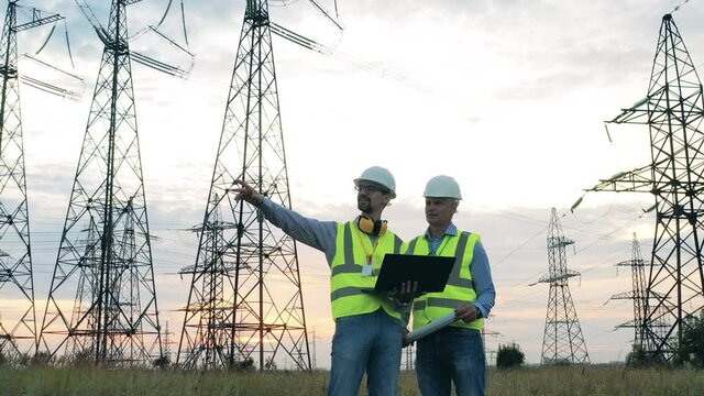Male engineers look at power poles in the field.