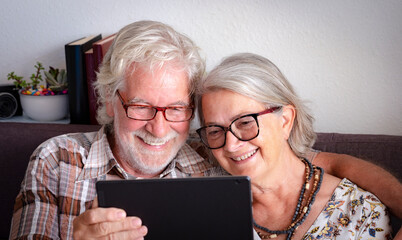 Happy senior couple with white hair and glasses in video call with family with a tablet - active retired elderly people social and tech at home