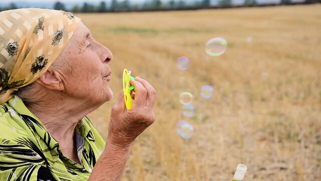 Old grandmother blowing soap bubbles. Conceptual photo of childhood and old age. Time is irreversible. Baby soap bubbles in old wrinkled hands of grandmother close-up. Happy grandmother