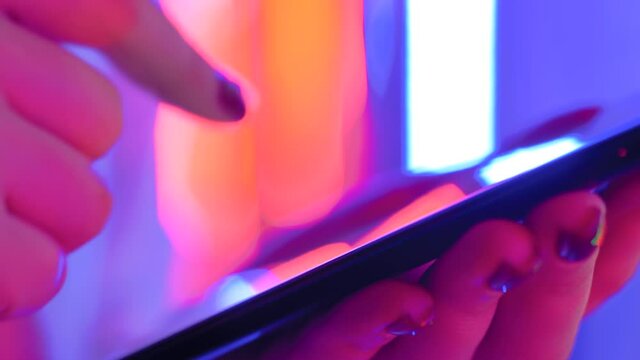 Woman using smartphone device at interactive exhibition or museum with purple illumination - scrolling and touching - close up side view. Futuristic, retrowave, immersive, entertainment concept