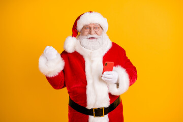 Fototapeta na wymiar Photo of excited grey white beard hair santa claus use smartphone raise fists celebrate x-mas christmas jolly holly lottery victory wear cap headwear isolated bright shine color background