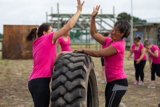Two woman high fiving each other over a tire at boot camp