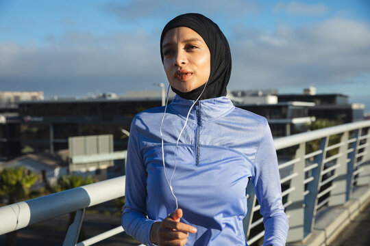 Woman in hijab listening to music while exercising on footbridge