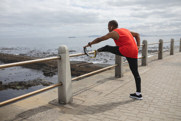 Black African American Man with prosthetic leg performing stretching exercise on the promenade