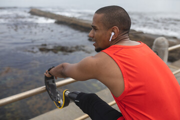Black African American Man with prosthetic leg performing stretching exercise on the promenade