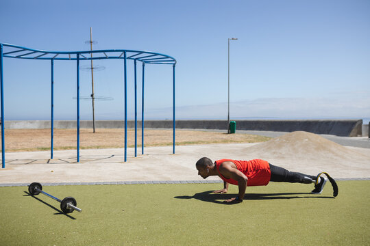 Black African American Man with prosthetic leg performing push up exercise in the park - Powered by Adobe