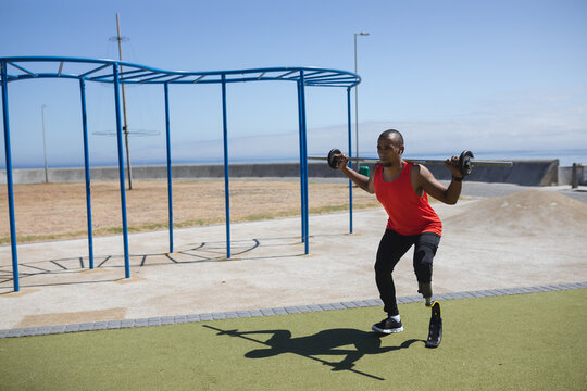 Black African American Man with prosthetic leg lifting weights on a barbell in the park