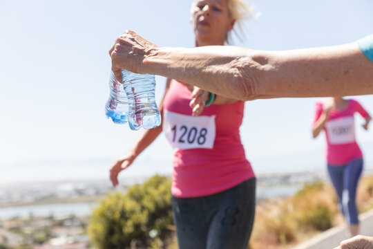 Mid section of woman giving water bottles to female runners