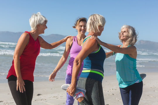 Smiling women performing stretching exercise on beach