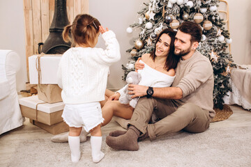 Obraz premium young parents with a small daughter against the background of the Christmas tree, Merry Christmas, family portrait