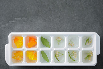 Ice mold with flowers preparing for freezing on the gray background.
