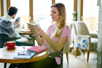 Focused young businesswoman watching tablet while resting in cozy cafe