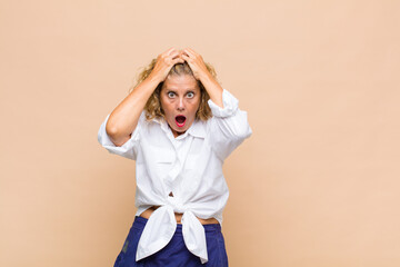 Middle age woman feeling horrified and shocked, raising hands to head and panicking at a mistake
