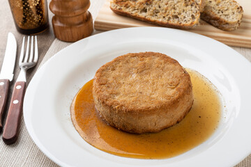 Breaded camembert cheese with honey, black pepper and grilled bread slices over wooden table